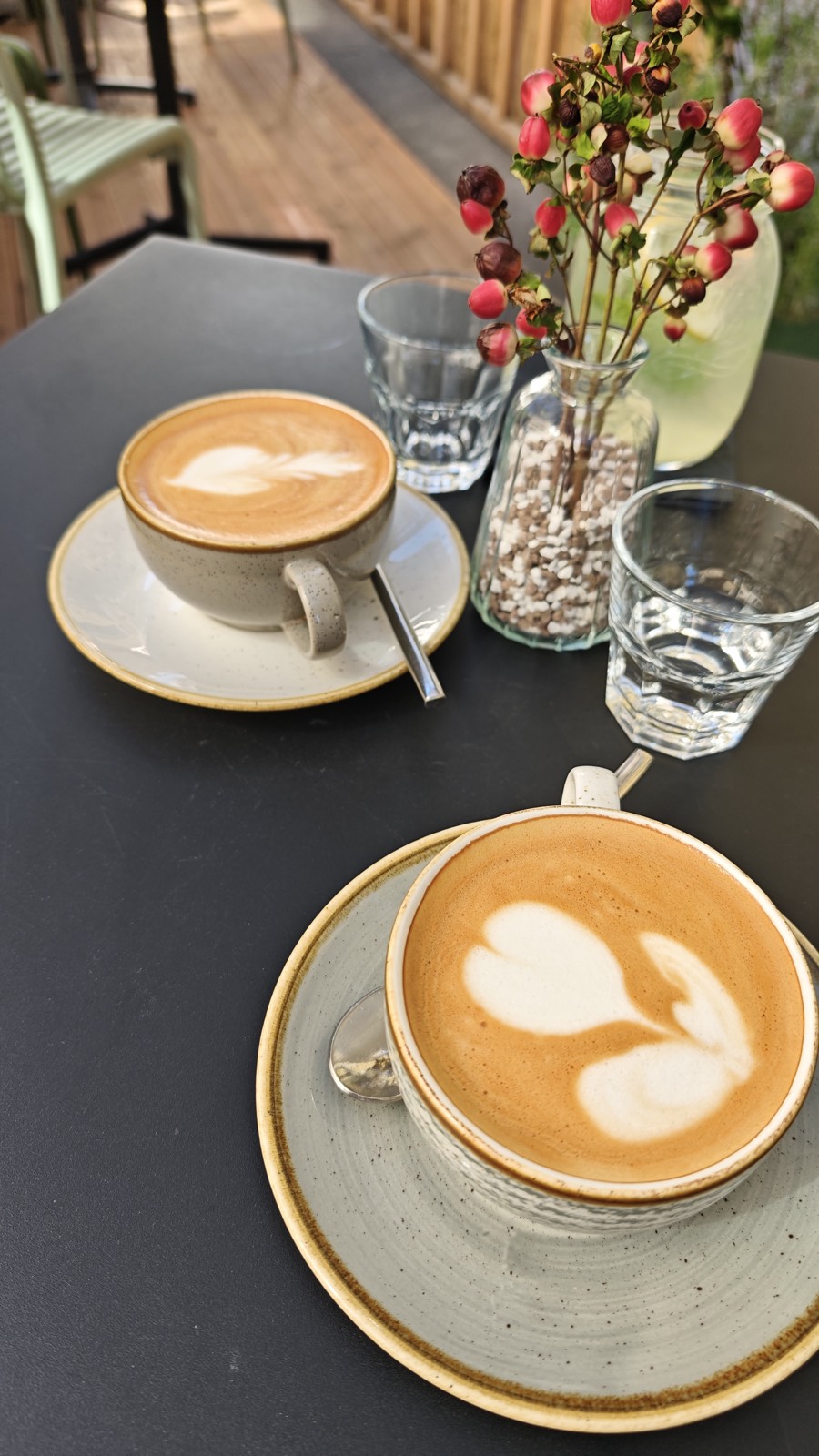 Zwei Cappuccini mit Latte Art auf einem Cafétisch mit Blumen